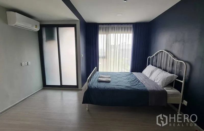 Condominium for rent in Phra Khanong, Bangkok - Spacious bedroom with blue feature wall, large window, and air conditioning.