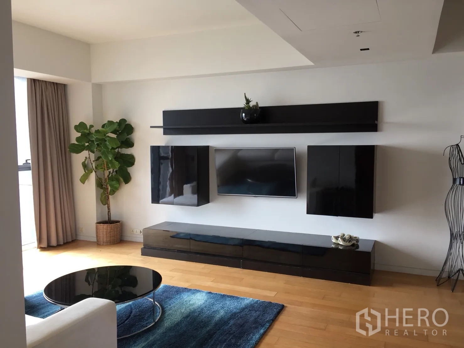 Condominium for rent or sale in Sathon, Bangkok - Bright living room with wall-mounted TV, black cabinetry, blue rug and wooden floors.