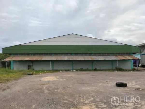 Warehouse for rent in Krathum Baen, Samut Sakhon - Rear view of the warehouse with a long corrugated awning and a large gravel loading yard.
