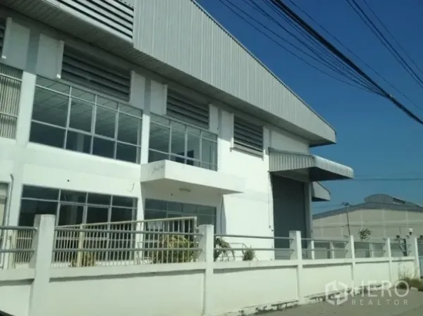 คลังสินค้า ให้เช่าในSamut Prakan - มุมมองด้านหน้าโกดังในสมุทรปราการ มีกำแพงรั้ว กระจกบานใหญ่ และประตูม้วนขนาดกว้าง