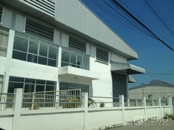 คลังสินค้า ให้เช่าในSamut Prakan - มุมมองด้านหน้าโกดังในสมุทรปราการ มีกำแพงรั้ว กระจกบานใหญ่ และประตูม้วนขนาดกว้าง