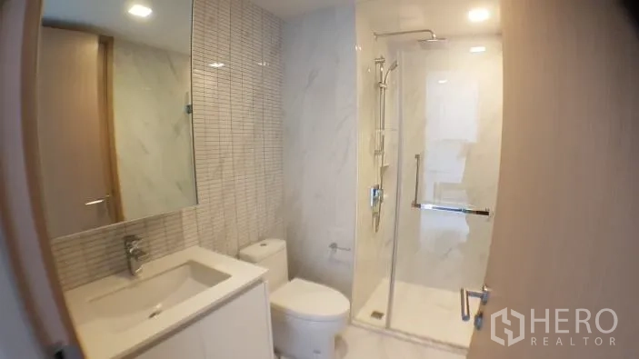 Condominium for rent in Watthana, Bangkok - Modern bathroom in the condominium with glass-enclosed shower, large mirror and white marble tiles.