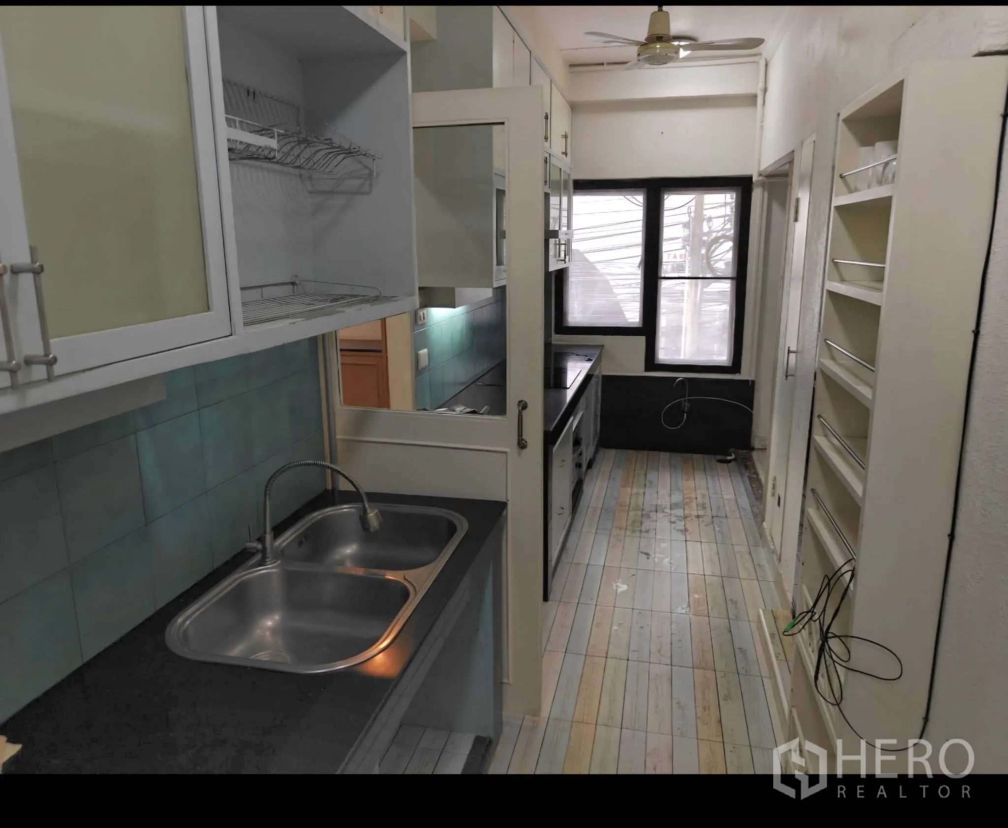 Condominium for rent in Sathon, Bangkok - Galley kitchen with double sink, upper cabinets with frosted glass, open shelving, and a window.