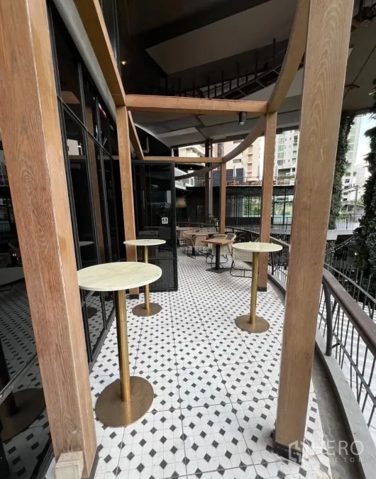 พื้นที่ขายปลีก ให้เช่า - ระเบียงทางเดินแคบพร้อมโต๊ะค็อกเทลสูง ใต้เสาไม้