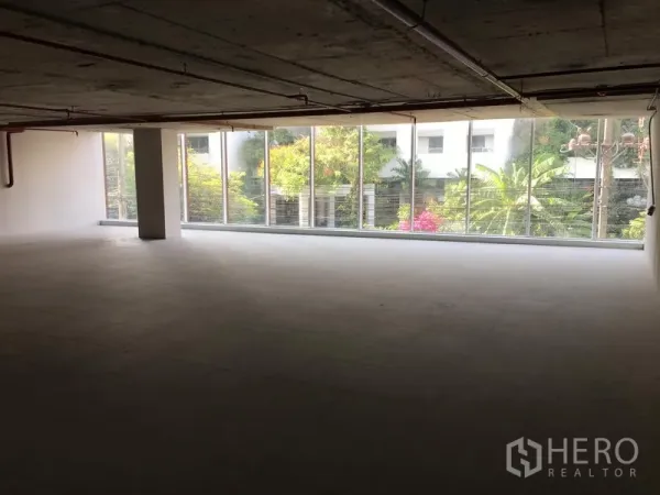 พื้นที่ขายปลีก ให้เช่าในKhlong Toei, Bangkok - พื้นที่ร้านค้ากว้างติดผนังกระจกยาว มองเห็นสวนภายนอก มีเสากลางและพื้นกระเบื้องเรียบ.