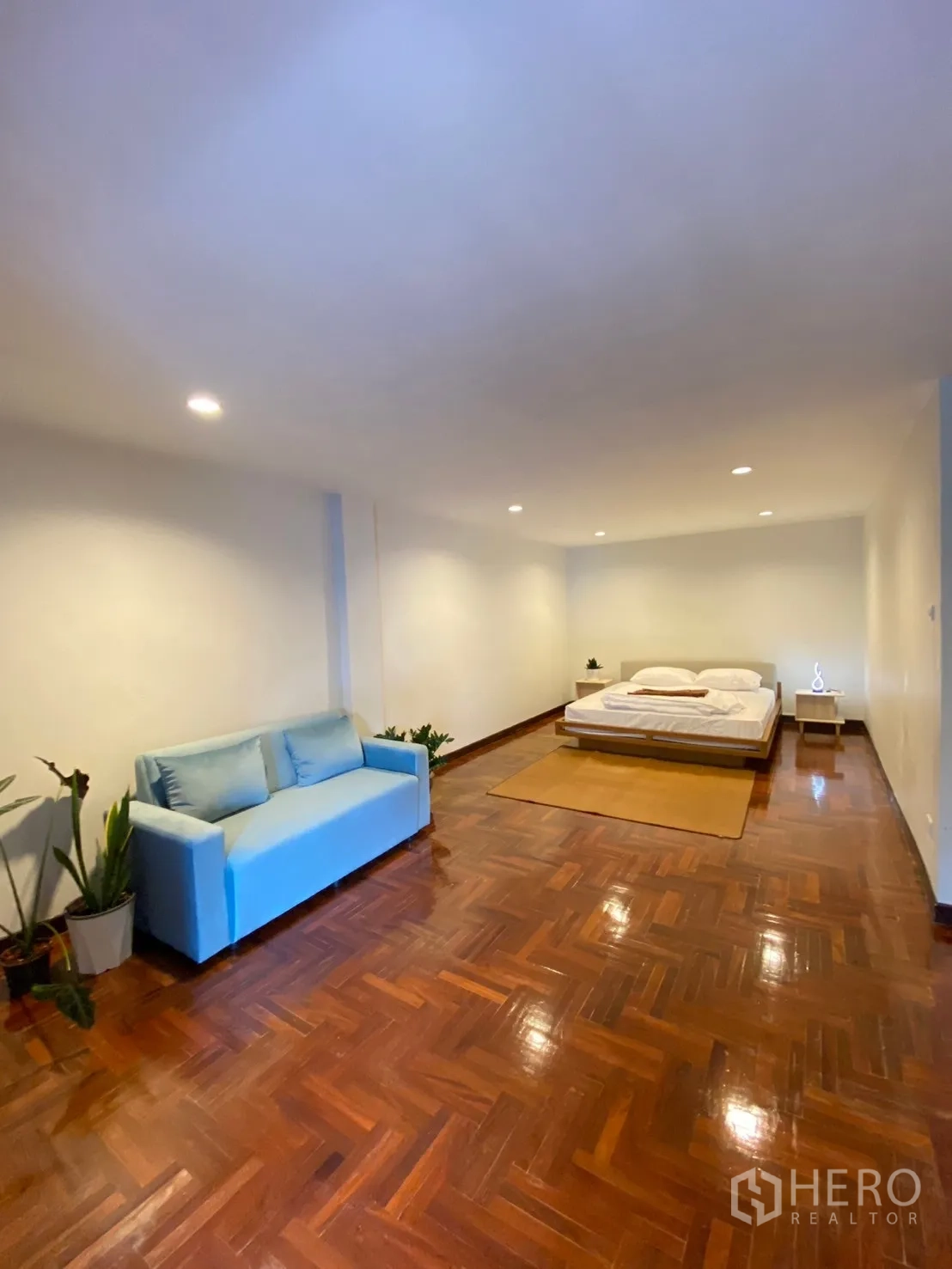 Home Office for rent in Watthana, Bangkok - Expansive bedroom featuring a blue sofa, platform bed and polished parquet flooring.