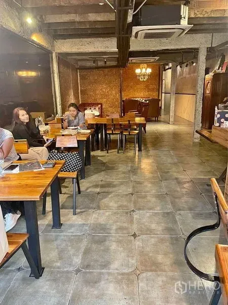 零售空间 出租在Phaya Thai, Bangkok - 工业风用餐区，木质餐桌、瓷砖地面、外露梁与吊灯，紧凑的阿里商铺室内。