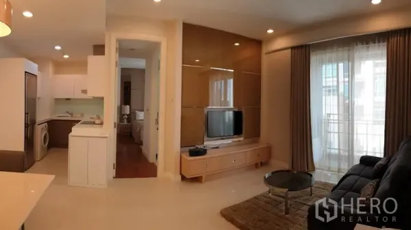 Condominium for rent in Pathum Wan, Bangkok - Open-plan living room with TV wall, balcony doors and view toward the kitchen and bedroom.
