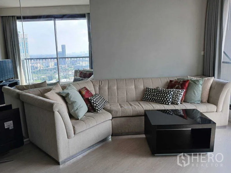คอนโด ให้เช่า - โซฟาเข้ามุมกับโต๊ะกลางเงาวาว ข้างหน้าต่างบานใหญ่เห็นวิวเมืองพาโนรามา