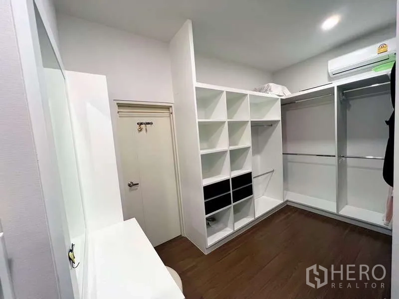 Detached House for sale in Prawet, Bangkok - Walk-in closet with white shelving, hanging rails, and a dressing counter beneath air conditioning.