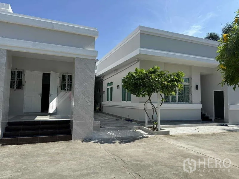 Detached House for rent in Samut Prakan - Single-storey modern house buildings with paved driveway and small trees.