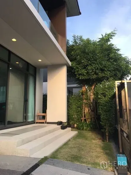Detached House for rent in Bang Kapi, Bangkok - Front steps and side garden with a mature tree beside the glass entry and tall windows.