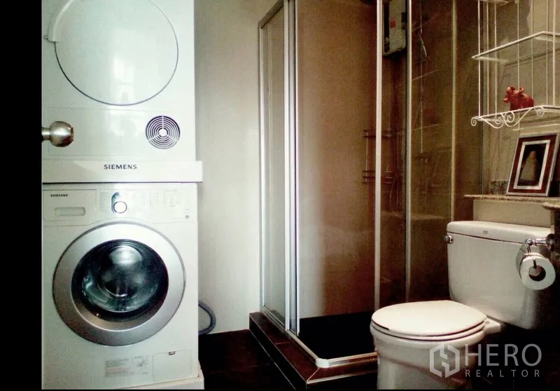Condominium for rent in Pathum Wan, Bangkok - Bathroom with stacked washer and dryer next to a glass shower enclosure.