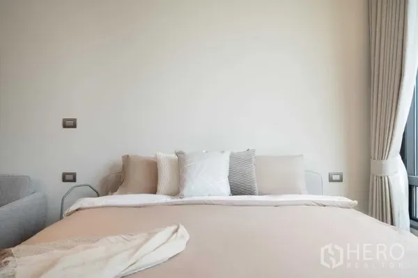 คอนโด ให้เช่าในPathum Wan, Bangkok - ภาพระยะใกล้ของเตียงปูผ้าสีเอิร์ธโทน หมอนตกแต่ง และผ้าม่าน สไตล์มินิมอล