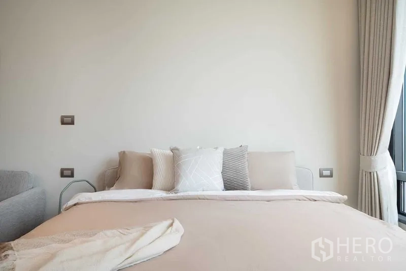 คอนโด ให้เช่าในPathum Wan, Bangkok - ภาพระยะใกล้ของเตียงปูผ้าสีเอิร์ธโทน หมอนตกแต่ง และผ้าม่าน สไตล์มินิมอล
