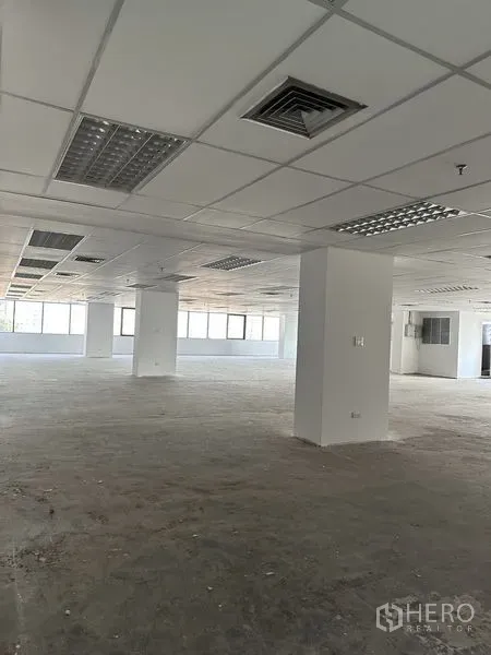 办公空间 出租在Pathum Wan, Bangkok - 空置办公室内景，网格吊顶、照明与通风口，结构柱清晰可见。