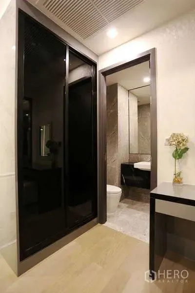 Condominium for rent in Watthana, Bangkok - Entry corridor with glossy black sliding wardrobe, vanity and doorway to bathroom.