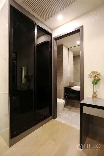 Condominium for rent in Watthana, Bangkok - Entry corridor with glossy black sliding wardrobe, vanity and doorway to bathroom.