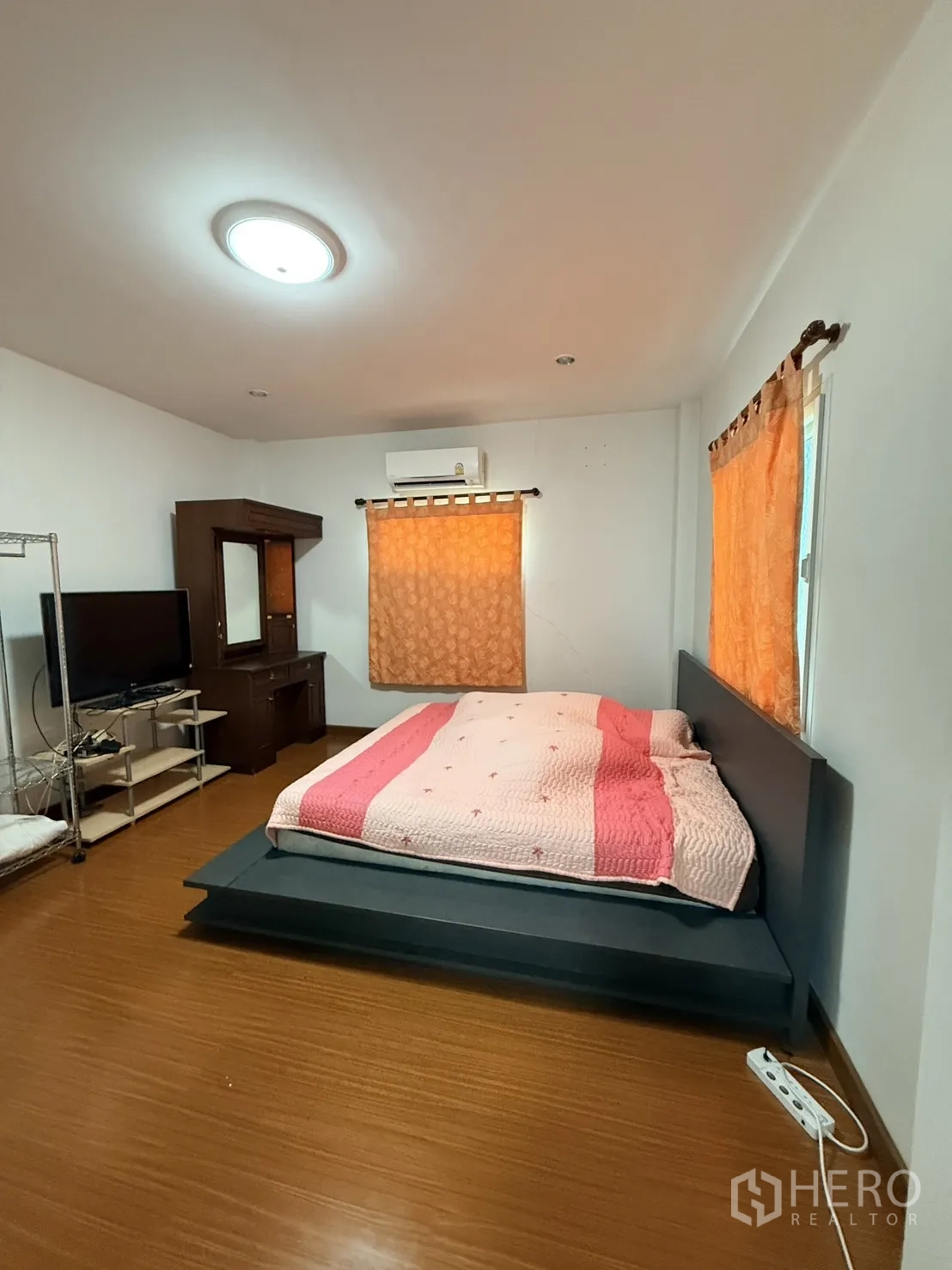 Detached House for rent in Lam Luk Ka, Pathum Thani - Spacious bedroom with platform bed, air-conditioning, and windows with curtains.