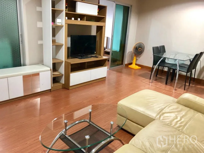 Condominium for rent in Huai Khwang, Bangkok - Open-plan living room featuring a leather sectional sofa, glass coffee table, TV unit, and dining set.
