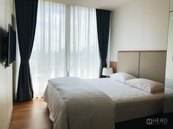 Condominium for rent in Khlong Toei, Bangkok - Bedroom with floor-to-ceiling windows, sheer and blackout curtains showcasing a city view.