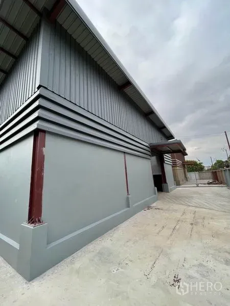 Warehouse for rent in Khlong Sam Wa, Bangkok - Side exterior showing roll-up door, paved loading yard, and modern metal cladding.