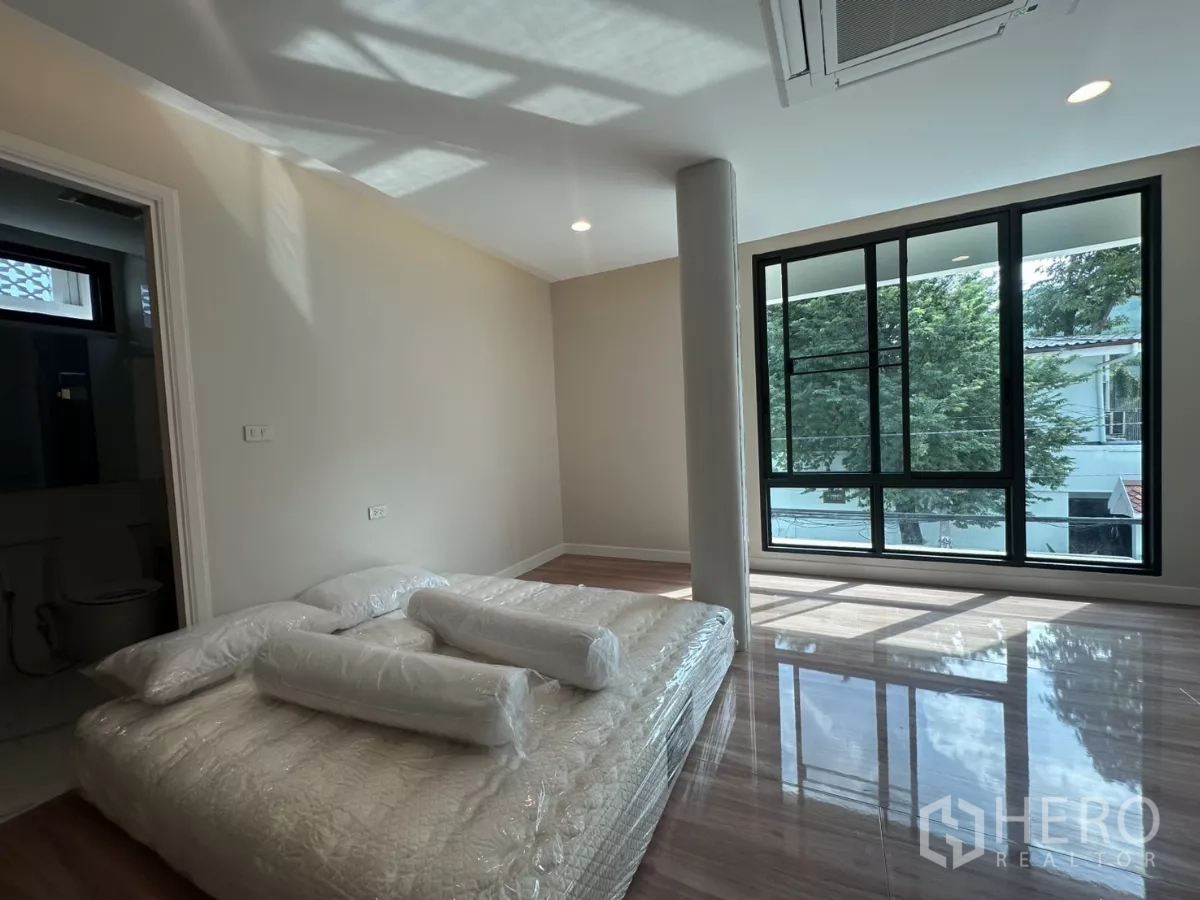 联排别墅 出租在Watthana, Bangkok - 转角卧室，大窗、绿树景观与临时床垫。