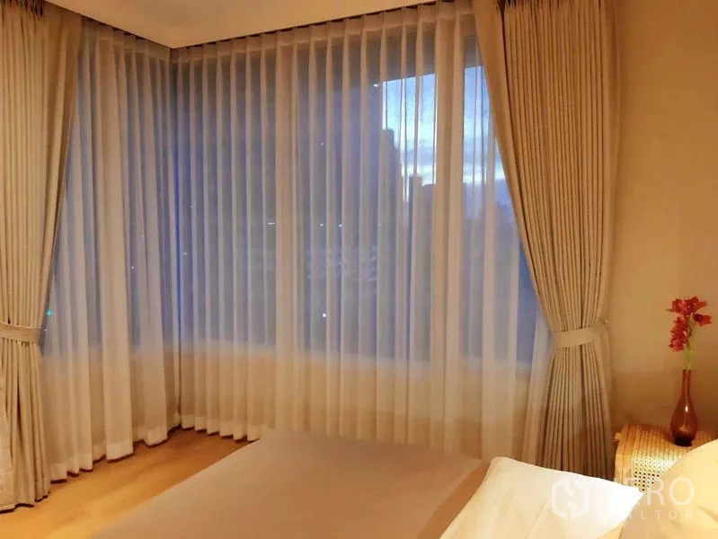 คอนโด ให้เช่าในRatchathewi, Bangkok - ห้องนอนช่วงค่ำ ม่านเต็มความสูง แสงไฟนุ่ม และวิวเมือง