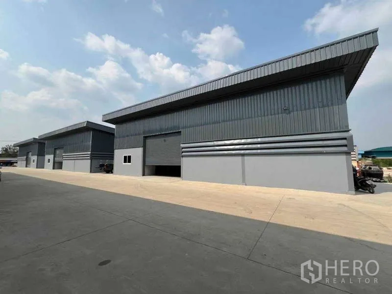Warehouse for rent in Pathum Thani - Long row of steel‑clad warehouses facing a broad access road under a partly cloudy sky.
