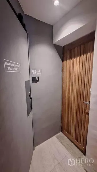 พื้นที่ขายปลีก ให้เช่าในWatthana, Bangkok - โถงทางหลังร้าน มีประตูเฉพาะพนักงานและป้ายบอกทางไปห้องน้ำ โทนสีเทามินิมอล