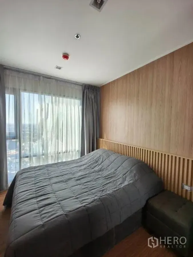 公寓 出租在Khlong Toei, Bangkok - 明亮卧室，落地窗与城市景观，灰色床品与木质墙面。