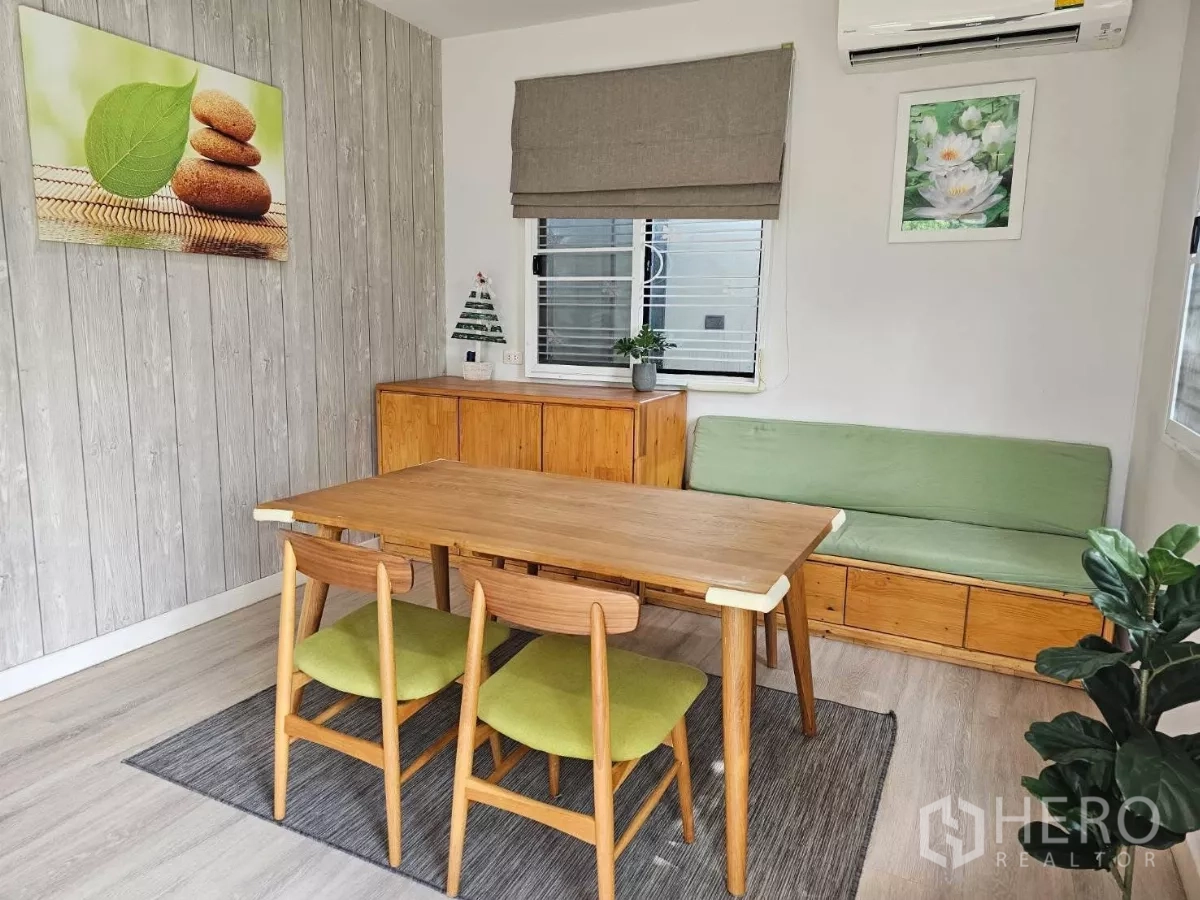 Detached House for rent or sale in Don Mueang, Bangkok - Dining area from another angle with wall art, air conditioner, and sideboard.