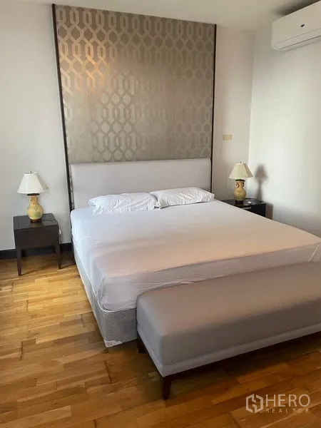 คอนโด ให้เช่าในPathum Wan, Bangkok - ห้องนอนหลัก เตียงคิงส์ไซส์ ม้านั่งปลายเตียง โคมไฟข้างเตียง และหัวเตียงลาย