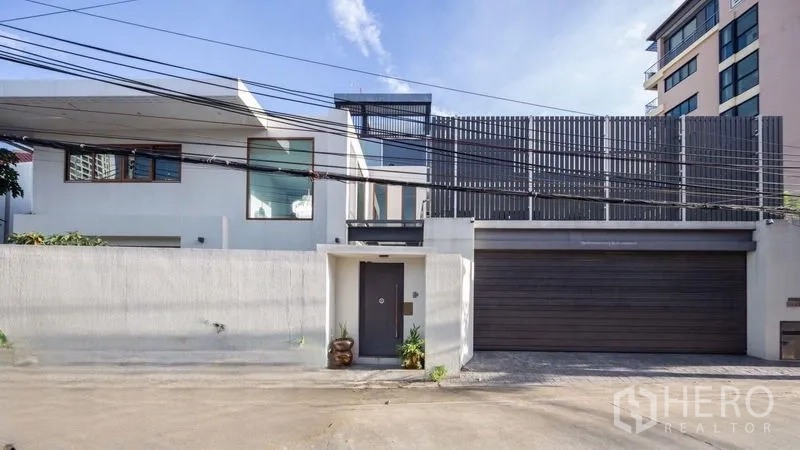 独立式住宅 出售在Chatuchak, Bangkok - 房屋正立面视角，宽大车库门与竖向遮阳格栅的现代外观。