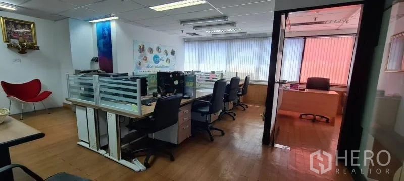 Office Space for rent in Watthana, Bangkok - Open-plan office with glass-partitioned workstations, wood flooring, ceiling lights, and a private room behind a glass door with window blinds.