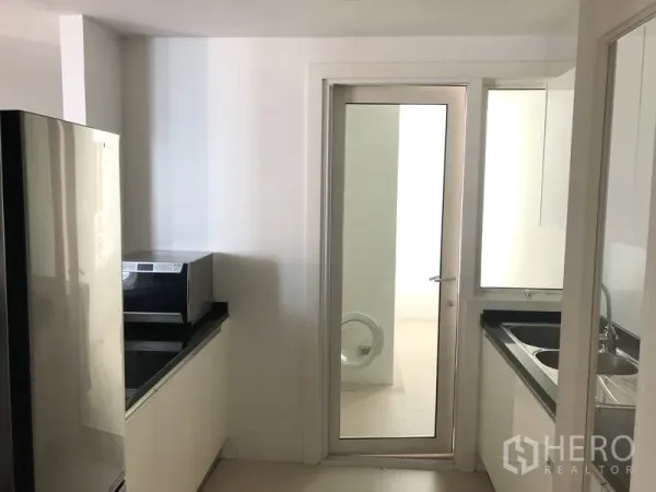 คอนโด ให้เช่าในKhlong Toei, Bangkok - ครัวปิดสว่างตา ตู้สีขาว เคาน์เตอร์สีดำ พร้อมประตูกระจกสู่พื้นที่ซักล้าง