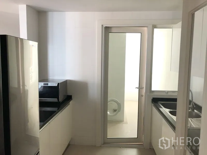 คอนโด ให้เช่าในKhlong Toei, Bangkok - ครัวปิดสว่างตา ตู้สีขาว เคาน์เตอร์สีดำ พร้อมประตูกระจกสู่พื้นที่ซักล้าง