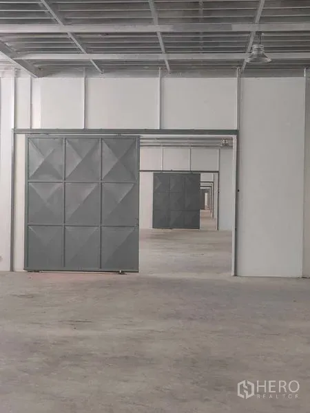 Warehouse for rent in Krathum Baen, Samut Sakhon - Interior corridor showing multiple steel sliding doors and concrete floor inside the warehouse.