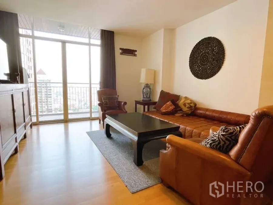 Condominium for rent or sale in Sathon, Bangkok - Cozy living room with leather sofa, coffee table, rug and sliding glass doors to a balcony with city view.
