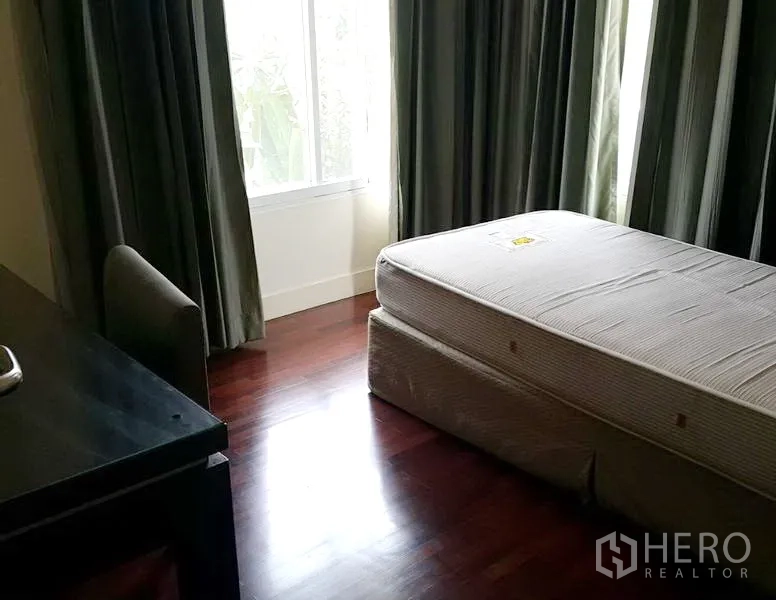 Detached House for rent in Wang Thonglang, Bangkok - Secondary bedroom with wood flooring, bed base, desk and large window with drapes.