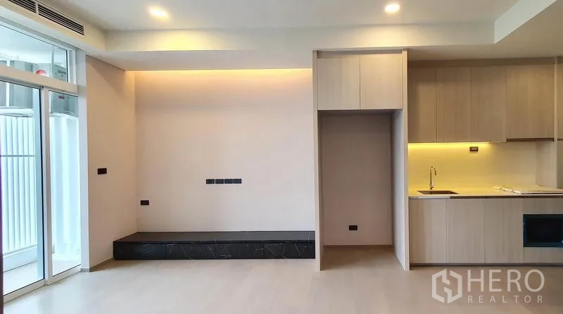 Condominium for sale in Khlong Toei, Bangkok - Living room with floor-to-ceiling windows beside an open kitchen with warm under-cabinet lighting.