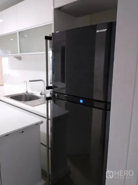 Condominium for rent in Pathum Wan, Bangkok - Kitchen corner featuring a glossy black refrigerator beside the sink and white upper cabinets.