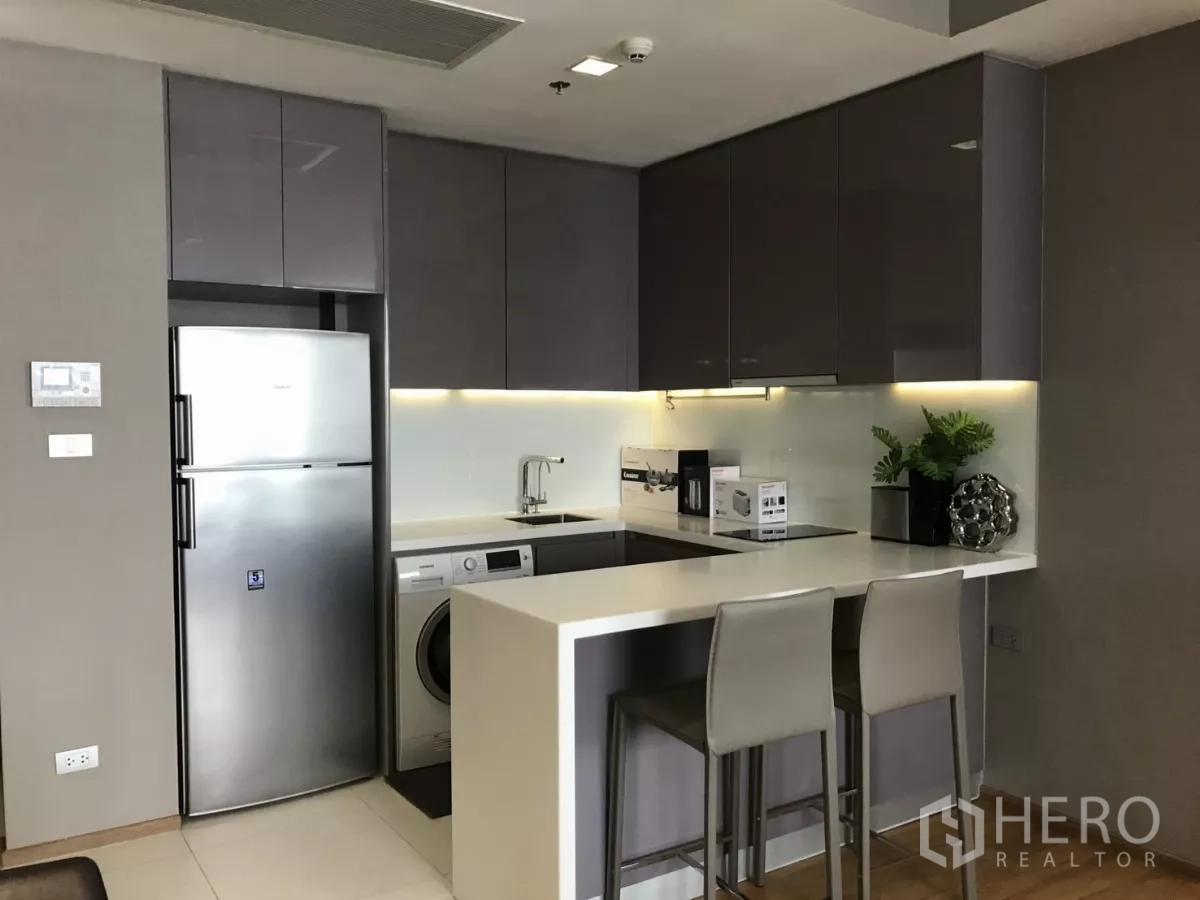 Condominium for rent in Watthana, Bangkok - Sleek corner kitchen with glossy cabinets, breakfast counter and built-in appliances.