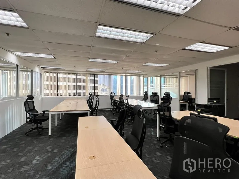 Office Space for rent in Khlong Toei, Bangkok - Bright open office with long bench desks and wide windows with blinds overlooking nearby towers.