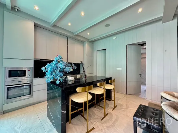 Detached House for rent or sale in Prawet, Bangkok - Contemporary kitchen with black marble island, gold stools and built-in ovens.