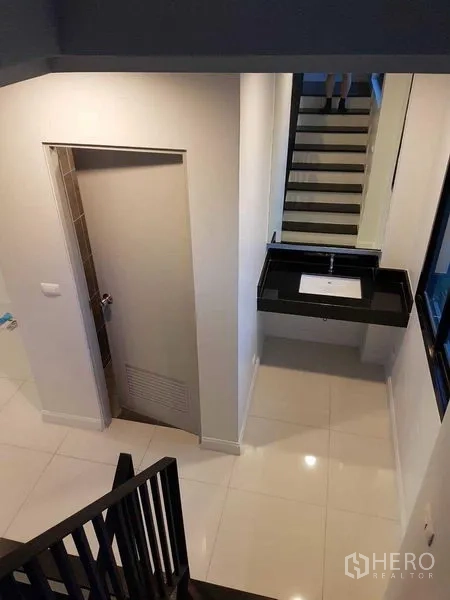 店屋 出租或出售在Bang Na, Bangkok - 楼梯平台视角，黑色楼梯、洗手台与房门。