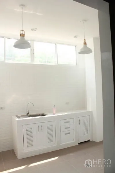 Home Office for rent in Khlong Toei, Bangkok - Bright white kitchenette with base cabinets, sink and twin pendant lights under high windows.
