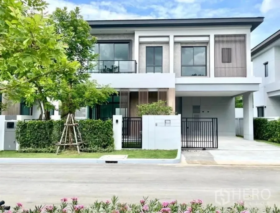 Detached House for rent or sale in Bang Phli, Samut Prakan - Front elevation of the modern house showing balcony, vertical slats, carport and trimmed hedges.