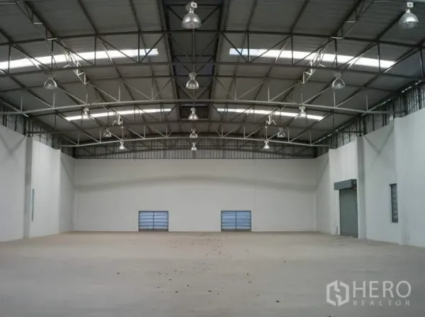 工厂 出租在Pathum Thani - 宽敞仓库内部，高挑钢桁架屋顶与采光天窗，混凝土地面。
