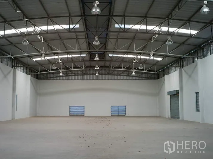 工厂 出租在Pathum Thani - 宽敞仓库内部，高挑钢桁架屋顶与采光天窗，混凝土地面。